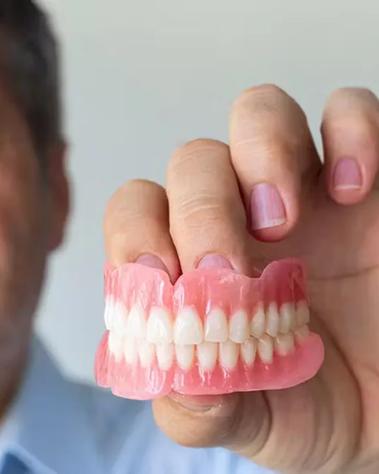 A man holding up a full set of upper and lower dentures in one hand