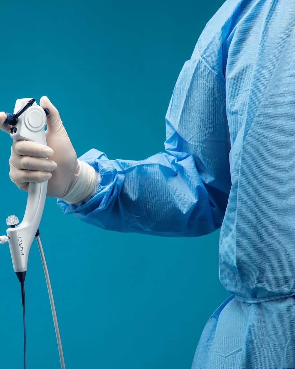 A gloved clinician in a blue gown holding an intraoral camera wand