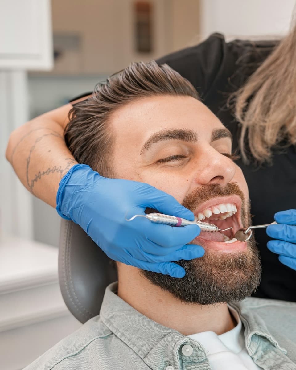 A smiling man reclined in a dental chair while a clinician in blue gloves works on his teeth